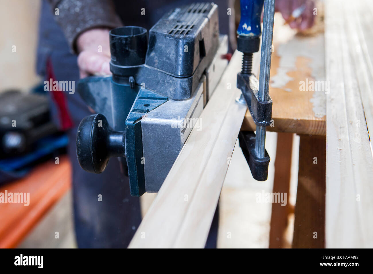 Carpenter lavora con i montanti delle porte tramite presa elettrica piano in posizione verticale Foto Stock