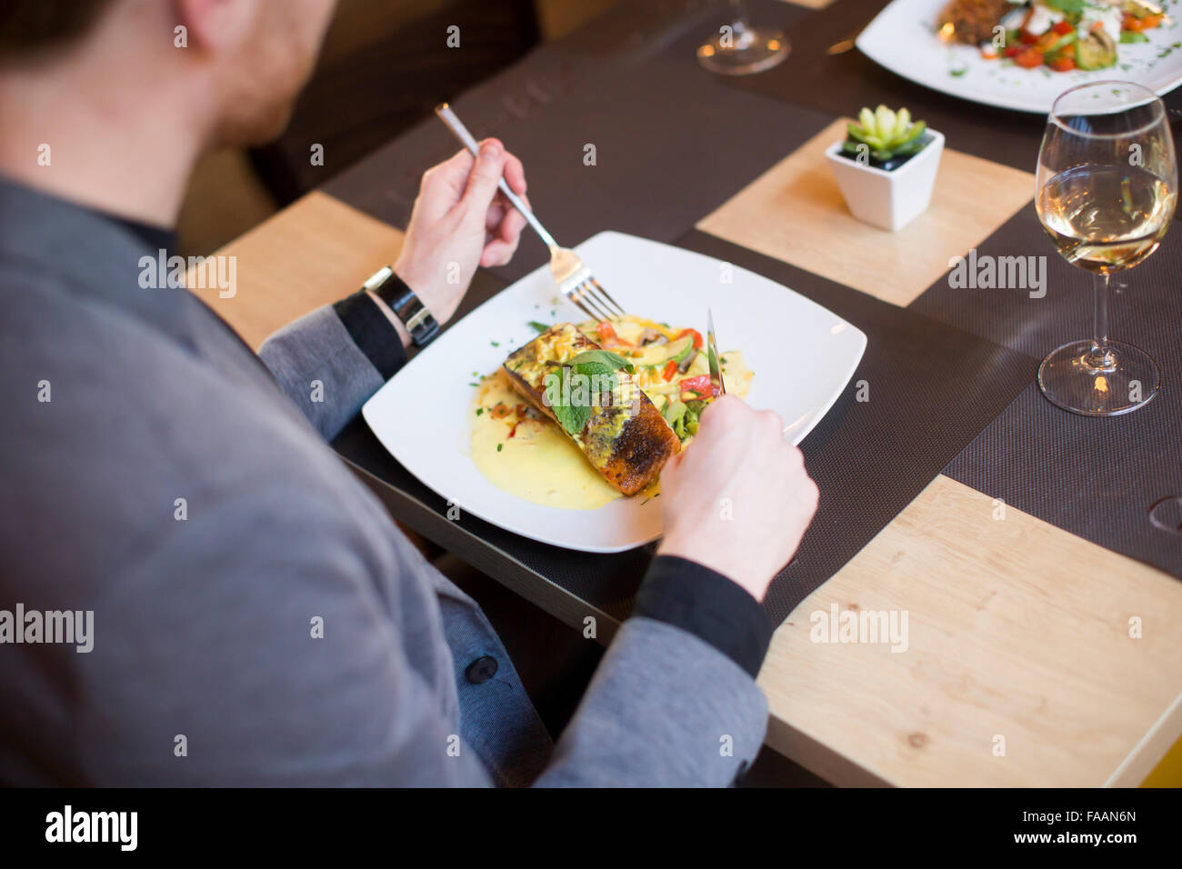 Giovane uomo mangiare salmone alla griglia con salsa di pomodoro e le erbe serviti presso il ristorante Foto Stock