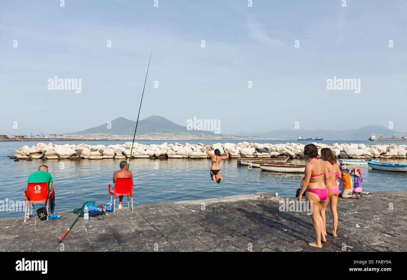 Napoli, Italia - 6 Maggio 2015: Gli adolescenti con un tuffo nel mare di Napoli city beach. Vulcano Vusuvius sullo sfondo Foto Stock