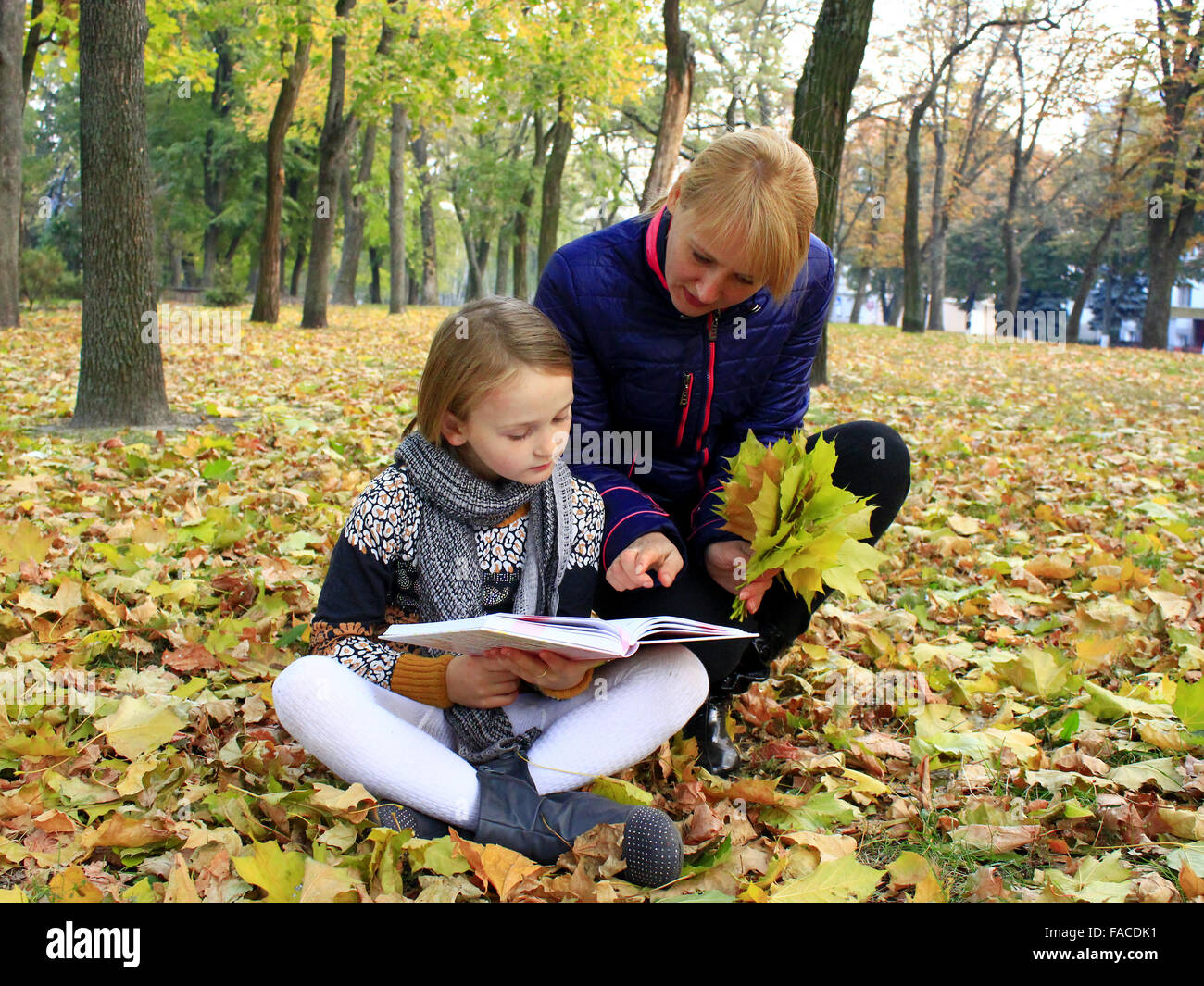 Madre e figlia di leggere un libro in autunno il parco della città Foto Stock