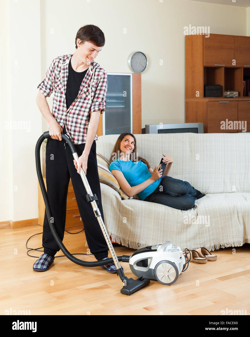 Giovane uomo di pulizia con aspirapolvere mentre la moglie giacente con  eBook su un divano a casa Foto stock - Alamy