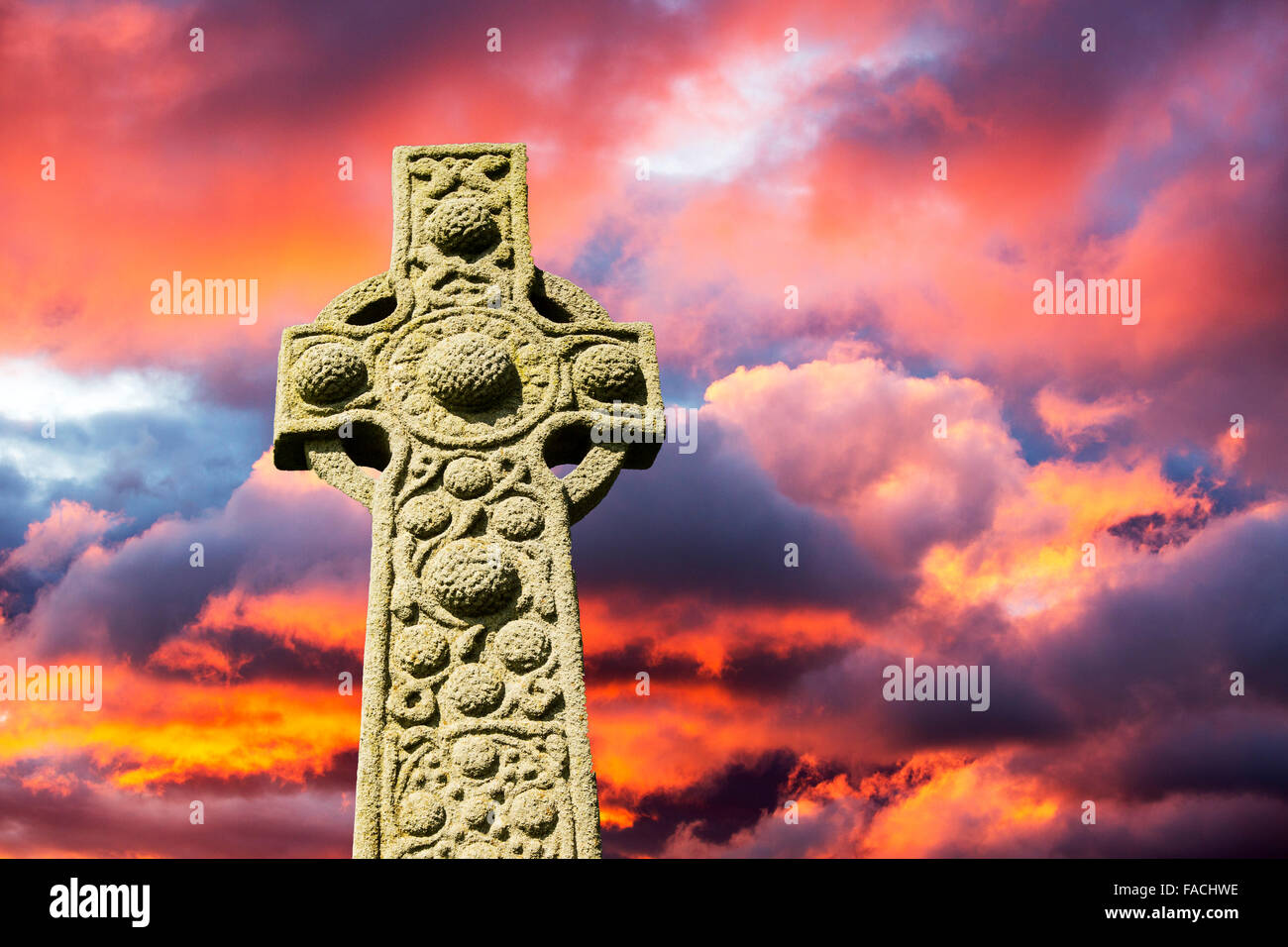 Un albero di striature di luce attraverso una lacuna nelle nuvole temporalesche al tramonto e una croce di pietra composita. Foto Stock