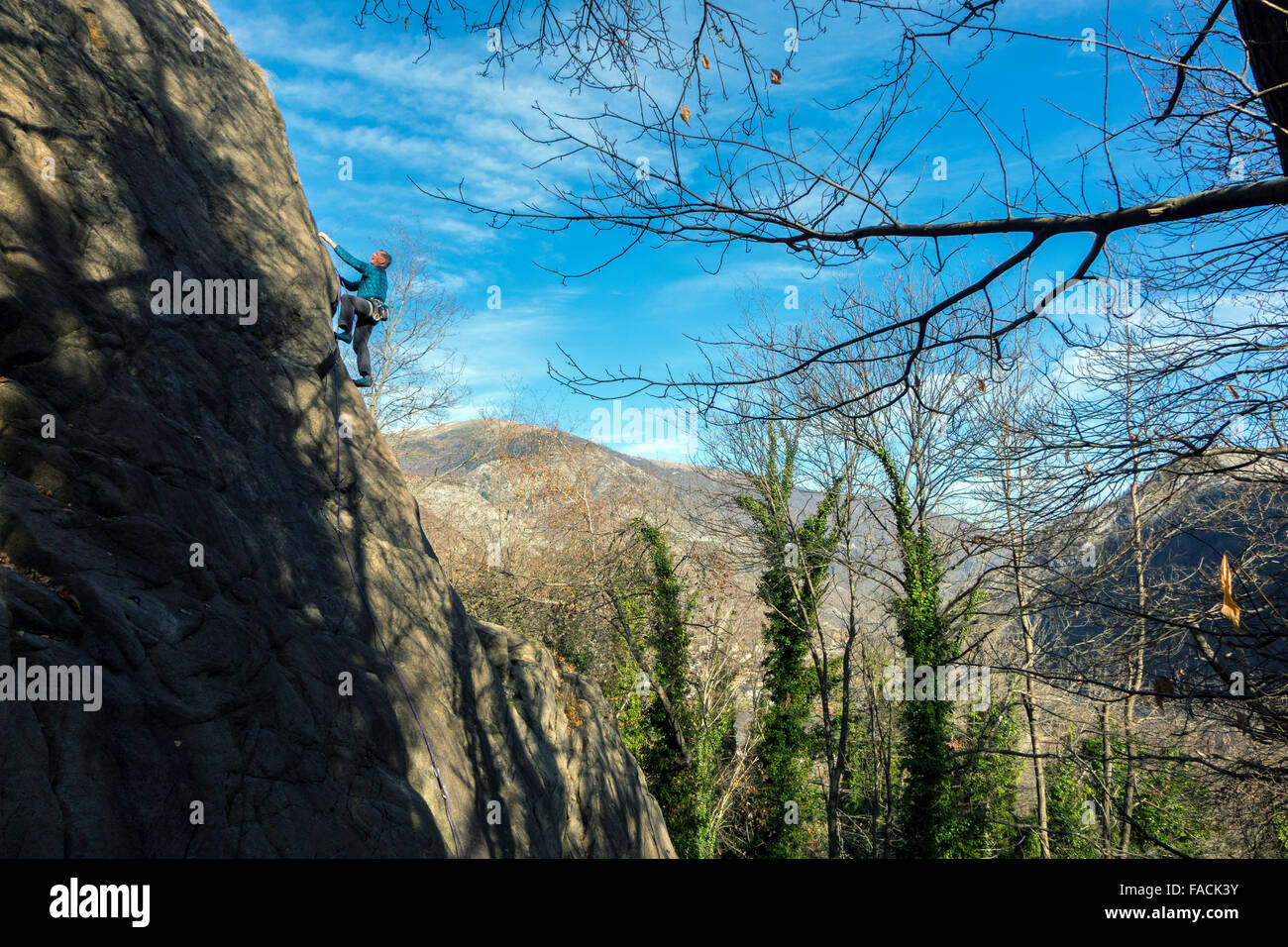 Maschio maturo rocciatore sulla scogliera con alberi e cielo blu Foto Stock