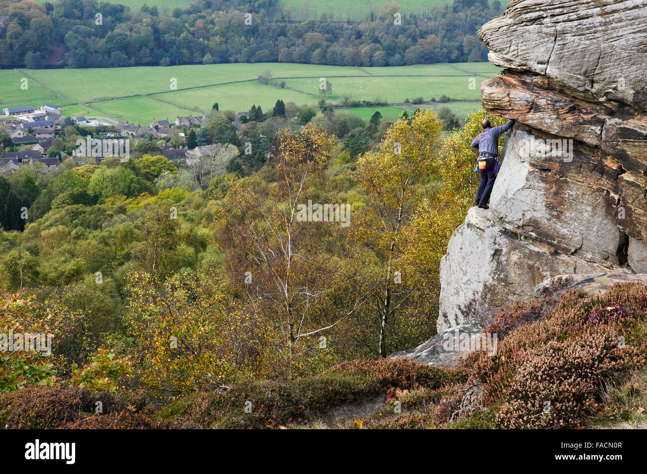 Un rocciatore sul bordo Froggatt nel Peak District, Derbyshire. Colore di autunno in alberi di seguito. Foto Stock