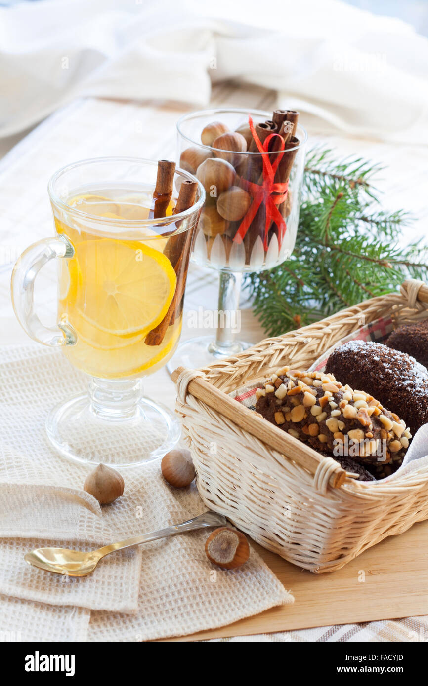 Caldo fresco tè verde nel bicchiere di vetro con limone e cannella, torte al cioccolato nel cestello e i dadi e la cannella in calice di vetro. Foto Stock