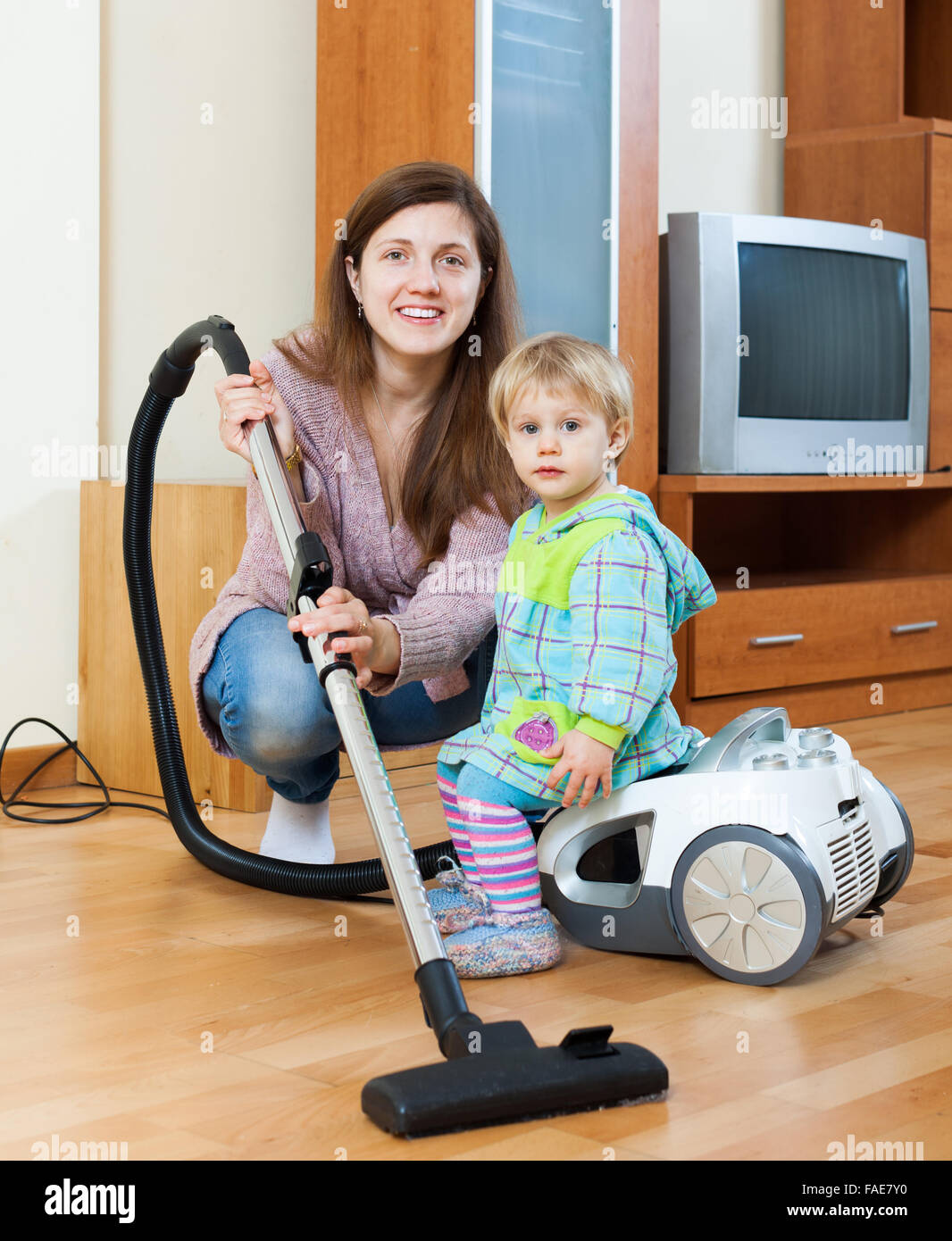 Felice madre con bambino pulizia stanza vivente con aspirapolvere Foto Stock