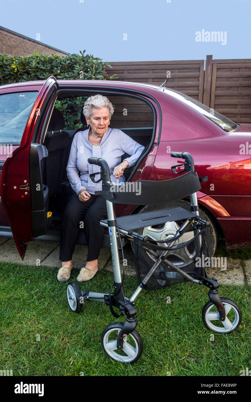 Donna anziana con rollator ruote / walker uscendo di auto sulla strada di casa Foto Stock