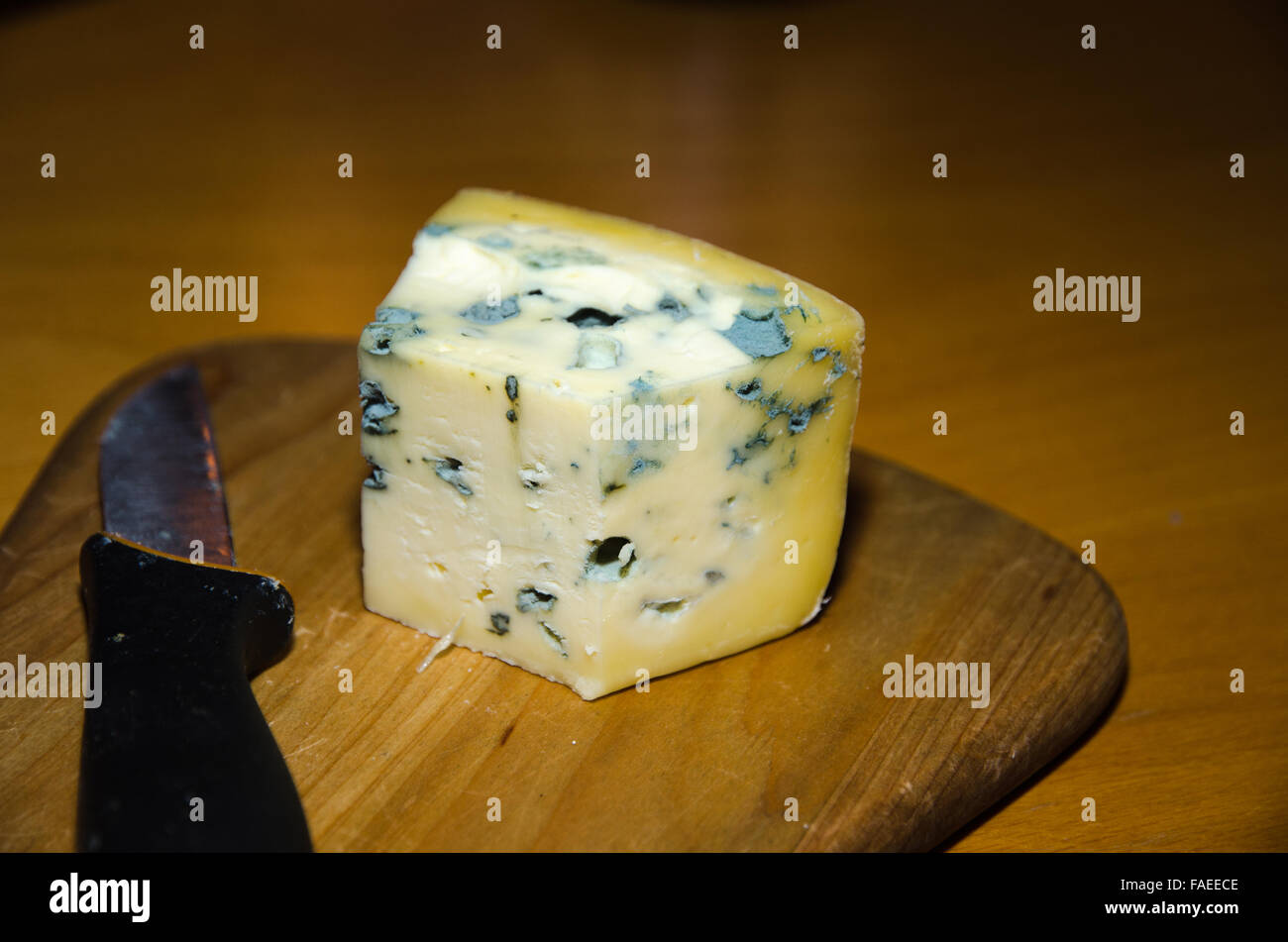 Close up di un pezzo di formaggio blu e i coltelli a un piatto di legno su un tavolo Foto Stock