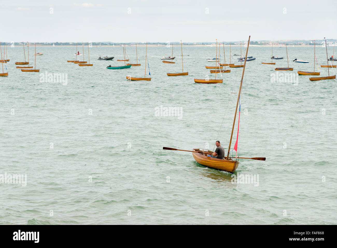 Un uomo che rema con una piccola barca a vela dinghy in mare al largo della costa di Seaview Isle of Wight REGNO UNITO su un nuvoloso giorno Foto Stock