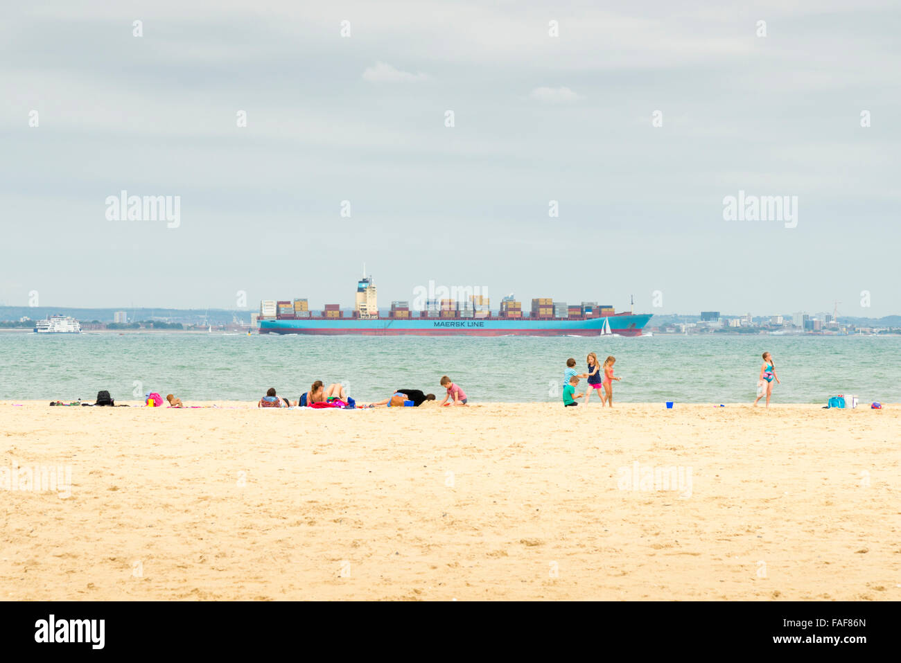 La gente a prendere il sole sulla spiaggia a Ryde Isle of Wight UK con un contenitore grande nave passando in mare Foto Stock