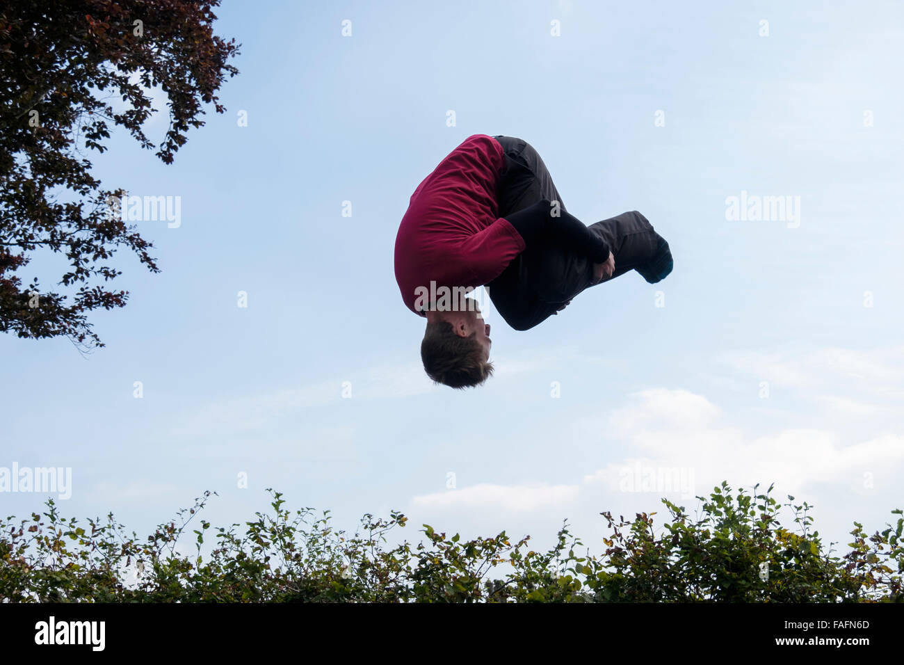 La millenaria uomo su un trampolino capovolto facendo un rollio in avanti capriola a metà in aria al di sopra di una copertura contro il cielo blu. Inghilterra, Regno Unito, Gran Bretagna Foto Stock