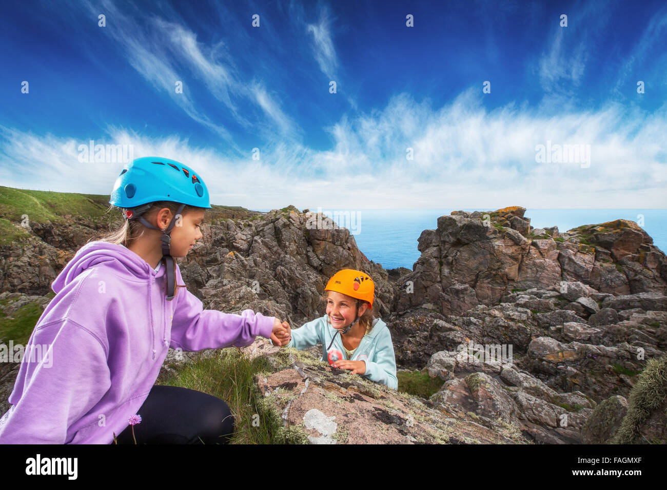 Un bambino aiuta un altro mentre alpinismo scogliere sul mare nei pressi di Aberdeen, Scozia, Regno Unito Foto Stock