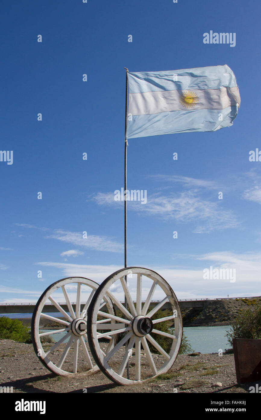 Bandiera dell'Argentina soffiando nel vento all aperto con ruote di carri contro il cielo blu in Patagonia. Foto Stock