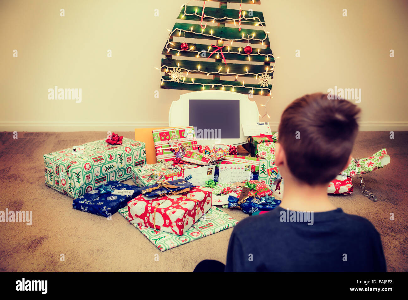 Ragazzo guarda i regali di Natale sotto un ecologico, riutilizzabili per albero di Natale Foto Stock