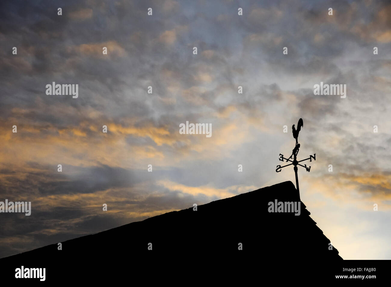Un segnavento stagliano sulla estremità di un tetto con un bellissimo cielo di sera. Foto Stock