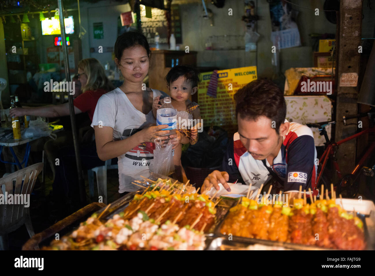 Famiglia street food fornitori in Khao San Road di Bangkok, Tailandia. Khaosan Road o Khao San Road è una breve strada nella zona centrale di Bangkok, Tailandia. È nella zona di Banglamphu di (Phra Nakhon distretto) circa 1 chilometro (0,62 mi) a nord del Grand Palace e del Wat Phra Kaew. "Khaosan' traduce come 'milled riso", un promemoria che in tempi passati la strada era un grande Bangkok mercato del riso. Negli ultimi venti anni, tuttavia, Khaosan Road ha sviluppato in una famosa in tutto il mondo "ghetto backpacker'. Esso offre sistemazione economica, da 'mattress in una scatola' style hotel a prezzi ragionevoli alberghi 3 stelle. Foto Stock