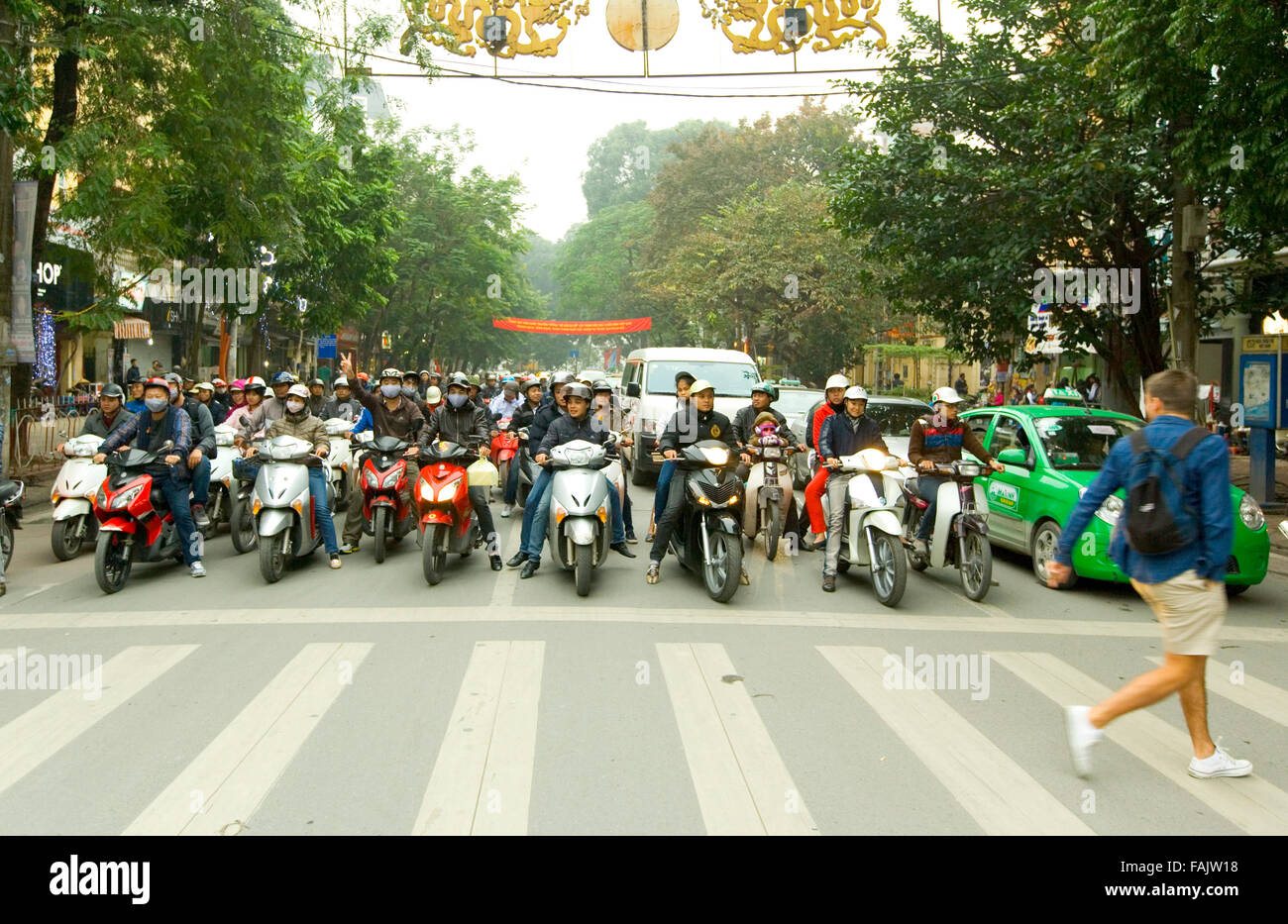 Uomo correre di fronte a persone in moto in Hanoi, Vietnam. Foto Stock