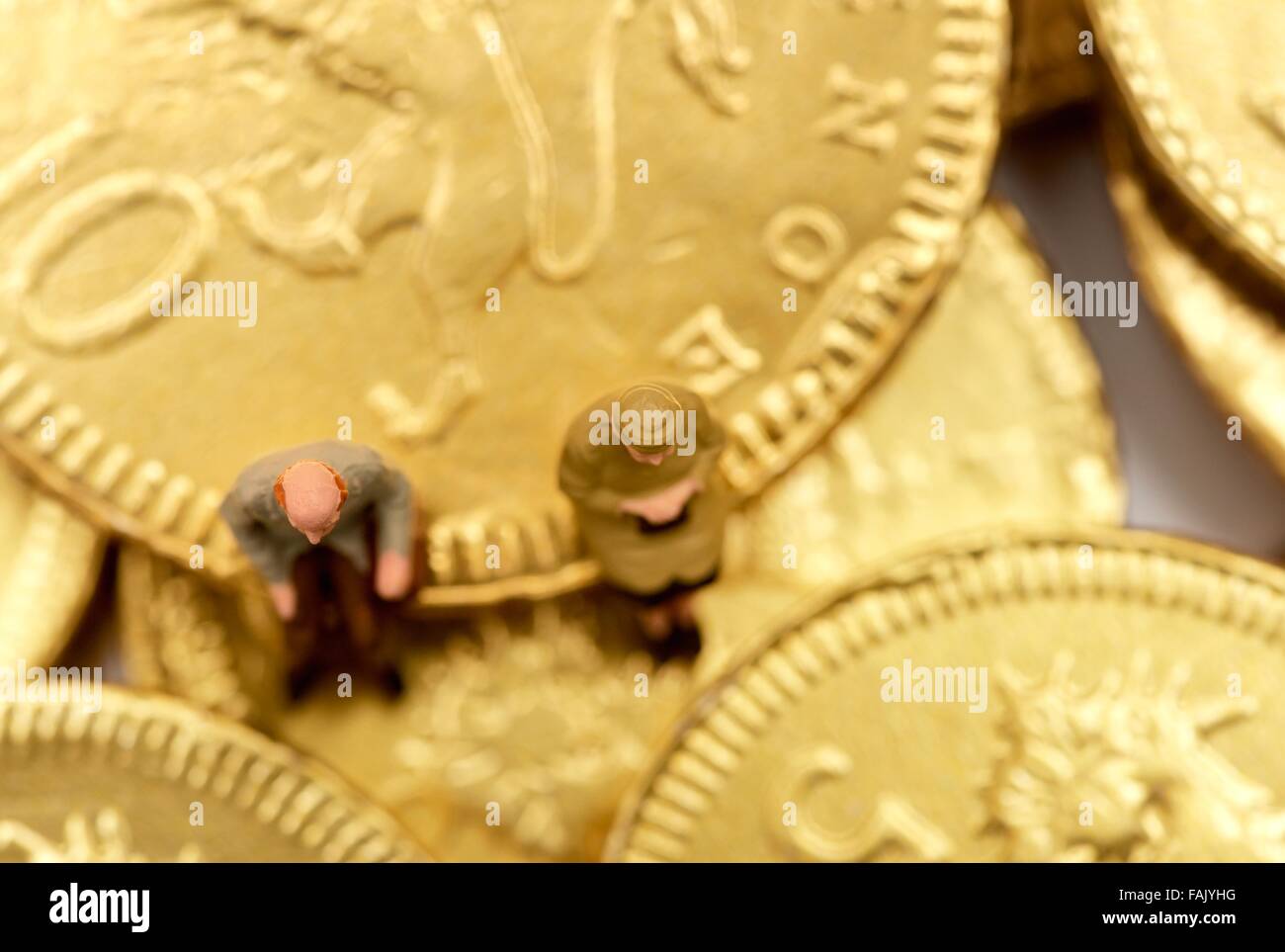 Miniatura gente seduta sul cioccolato monete di denaro Foto Stock