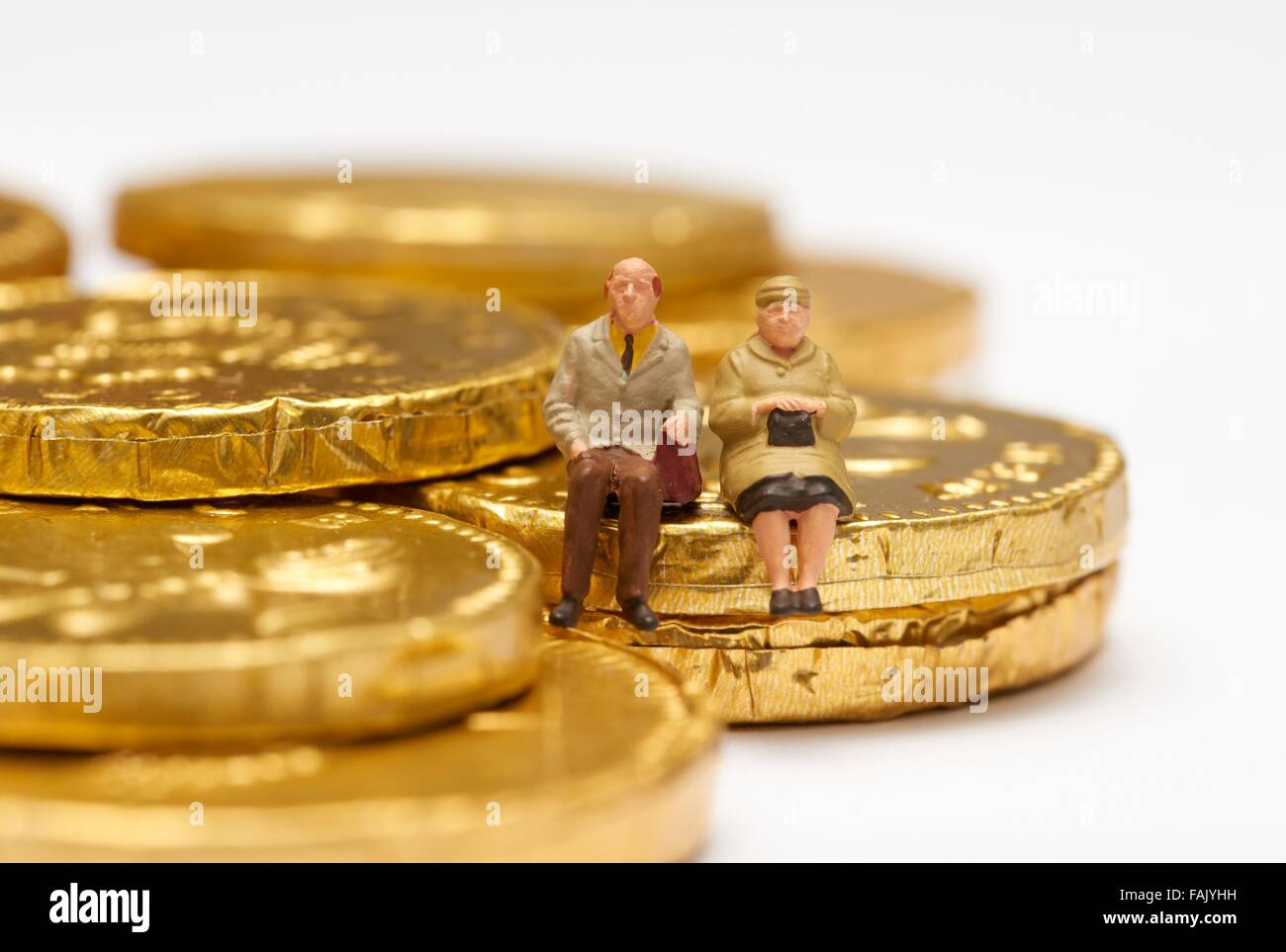 Miniatura gente seduta sul cioccolato monete di denaro Foto Stock