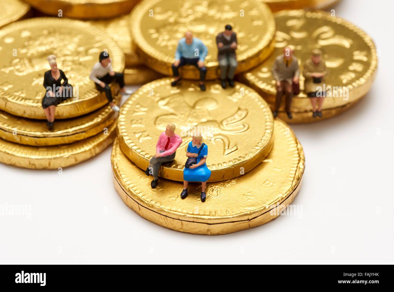 Miniatura gente seduta sul cioccolato monete di denaro Foto Stock