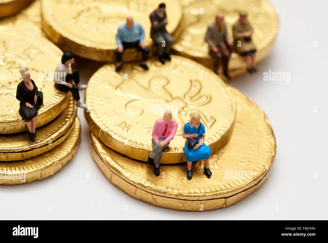 Miniatura gente seduta sul cioccolato monete di denaro Foto Stock