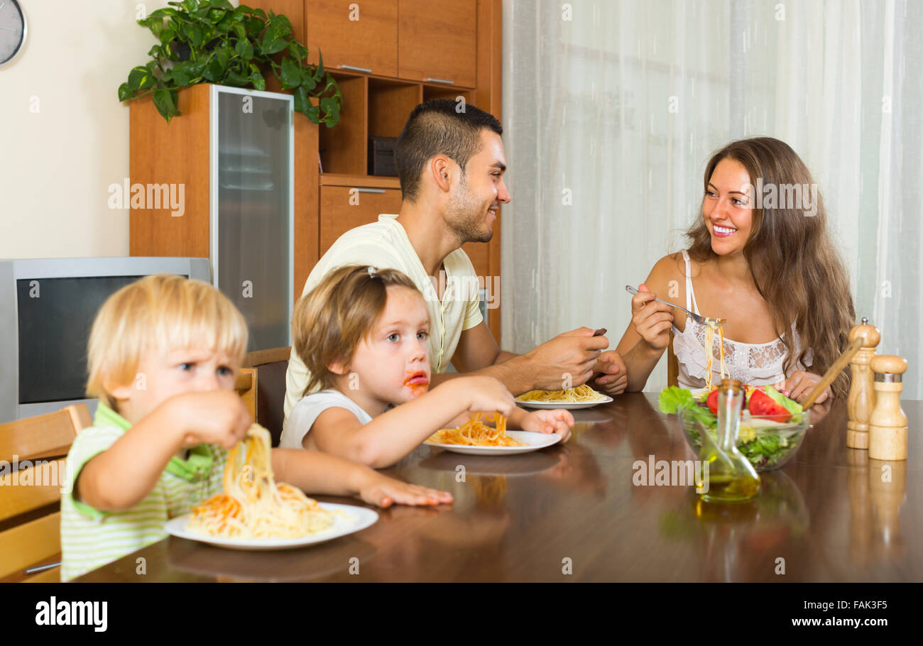 Felice famiglia giovane di quattro mangiare con gli spaghetti al tavolo Foto Stock