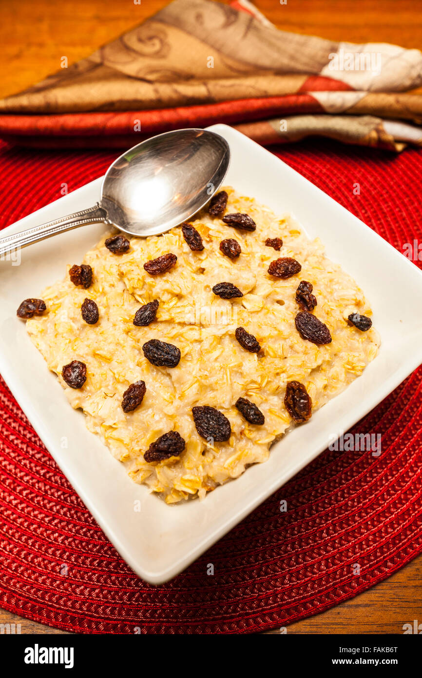 Una tazza di farina di avena con uvetta e cannella su un round cartellone su un tavolo di legno Foto Stock