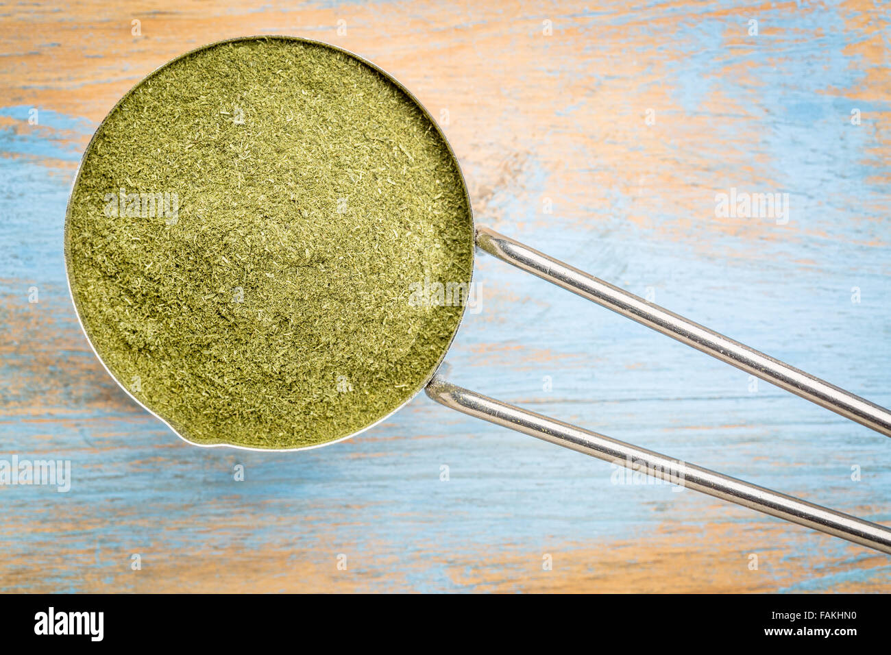 Green liofilizzata organic erba di frumento polvere, supplemento nutrizionale su un metallo misurino contro dipinta legno grunge Foto Stock