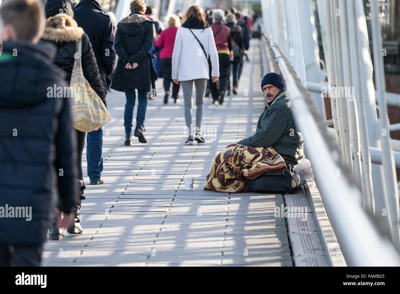 Le persone camminare davanti a un uomo senza tetto a mendicare per Hungerford Bridge di Londra. Foto Stock