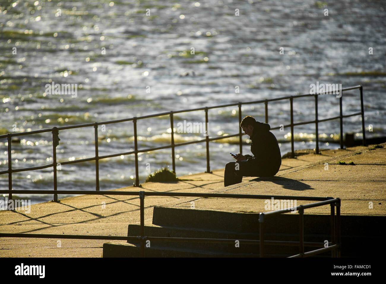 Silhouette di un uomo seduto in serata la luce del sole - un uomo seduto in tarda serata la luce del sole che si affaccia l'estuario del Tamigi. Foto Stock