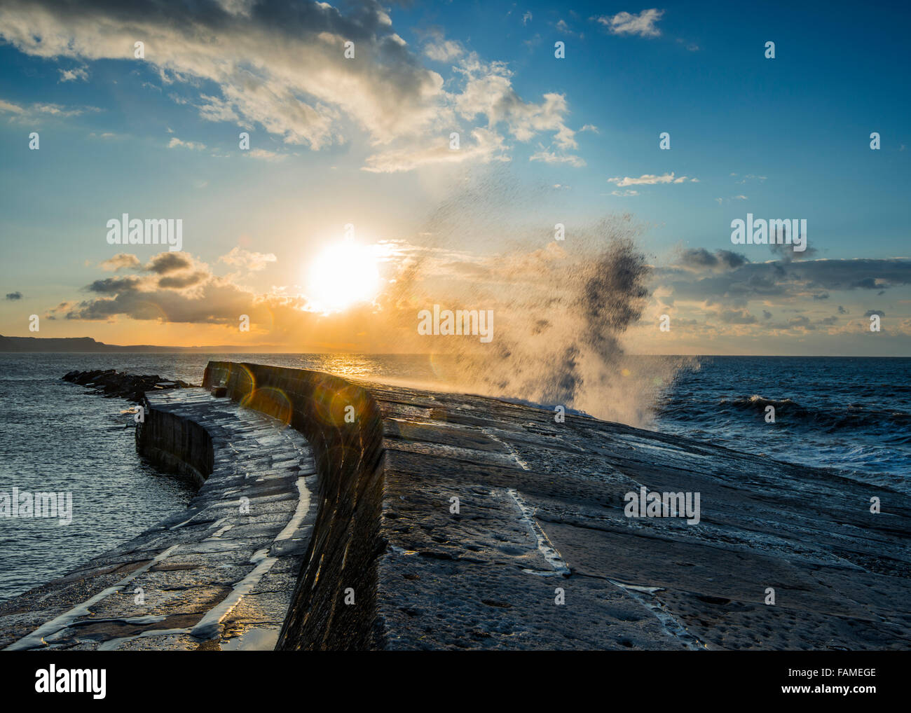 Sunrise over Lyme Regis bay, come un'onda rompe contro il Cobb. Foto Stock