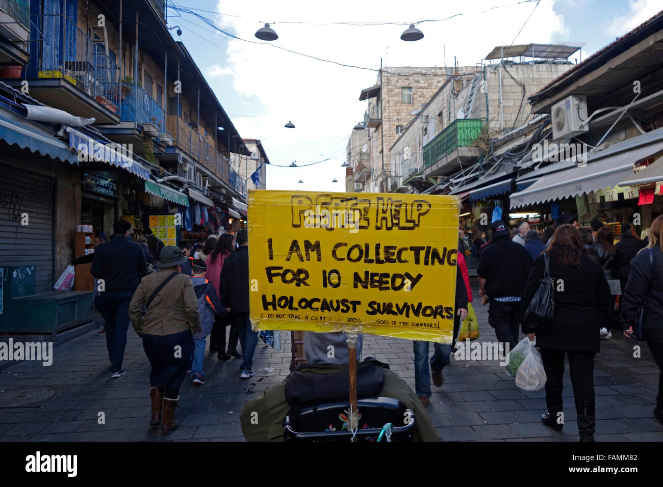 Un mendicante tiene un cartello che legge prego aiuto sto raccogliendo per 10 superstiti bisognosi dell'olocausto in Mahane o mercato di Machane Yehuda spesso indicato come 'lo Shuk', un mercato all'aperto, in Gerusalemme ovest, Israele Foto Stock