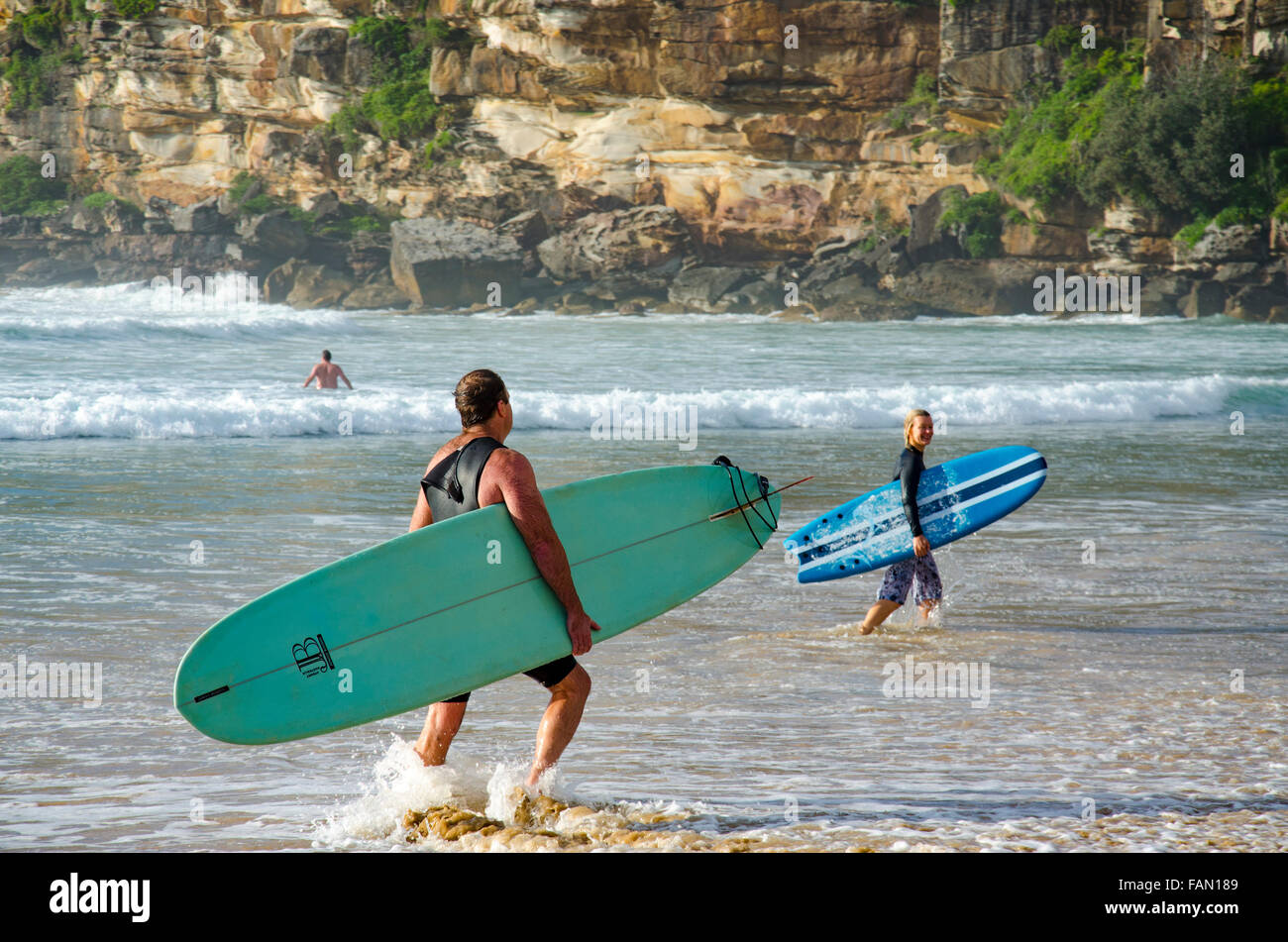 Un uomo e una donna surf board rider lasciare l'acqua in una soleggiata Sydney mattina a Freshwater Beach in Australia Foto Stock