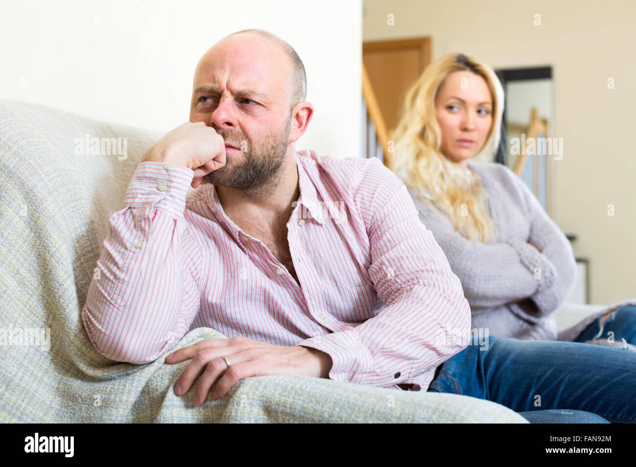Resenting adulto uomo seduto su un divano si è allontanata dal suo compagno di anima che è guardando lui reproachfully Foto Stock