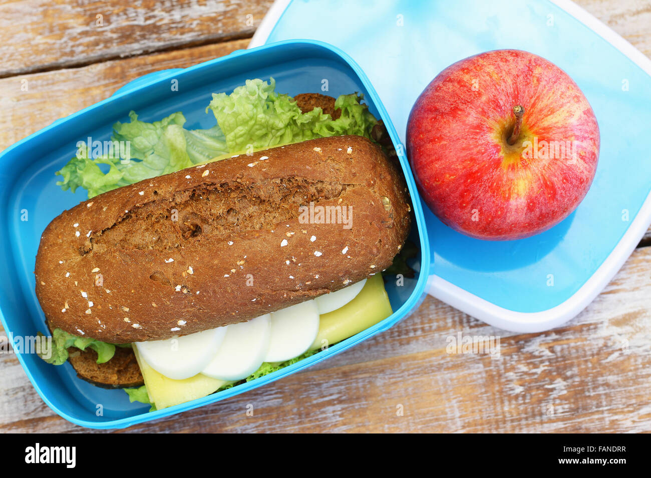 Pranzo sano scatola contenente marrone Rotolo di pane con formaggio, uovo sodo e lattuga e mela rossa Foto Stock