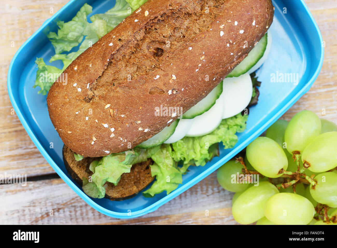 Scatola di pranzo contenente pane marrone rotolo con uovo sodo, formaggio e lattuga e uva Foto Stock