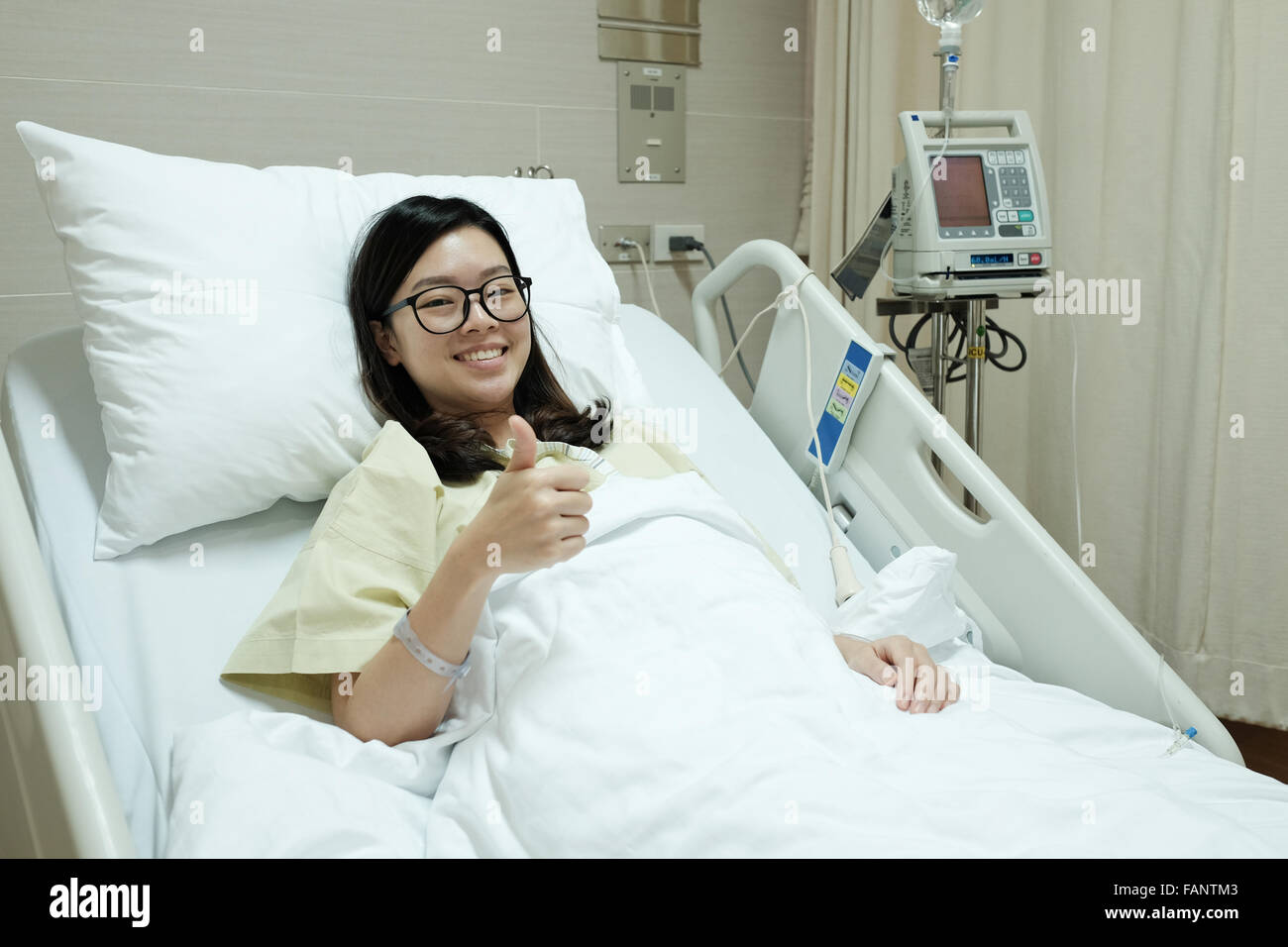 Pazienti asiatici girl Thumbs up e sorriso mentre giaceva sul letto di ospedale Foto Stock
