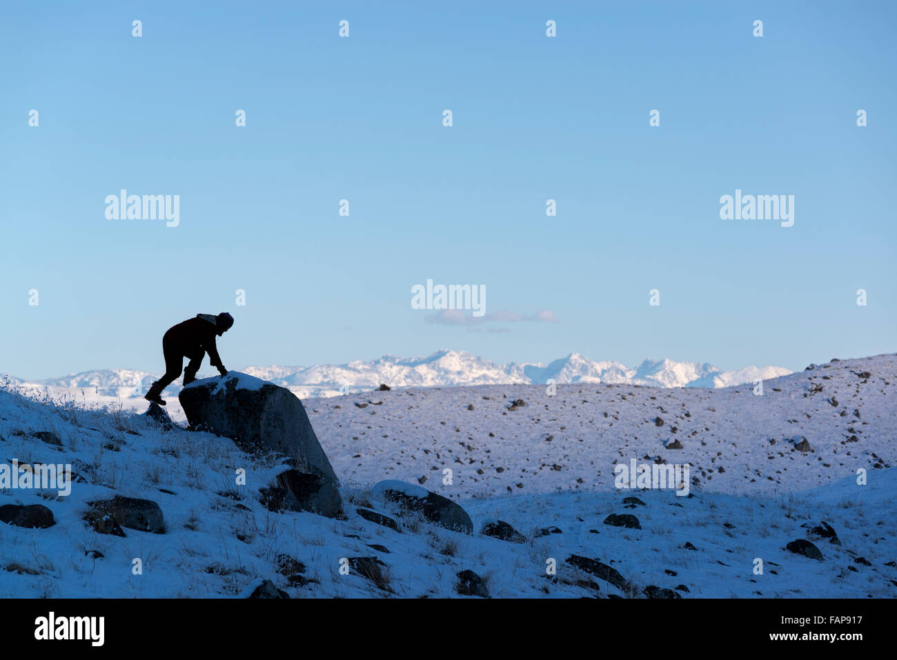Escursionista salendo su un masso su Oregon Wallowa del Lago Moraine in inverno con Idaho sette demoni montagne sullo sfondo. Foto Stock