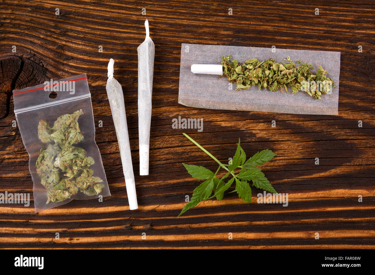 Sfondo di marijuana. La Cannabis joint, Bud in sacchetto di plastica e la canapa lascia su di un tavolo di legno. Coinvolgente Farmaco o medicina alternativa Foto Stock
