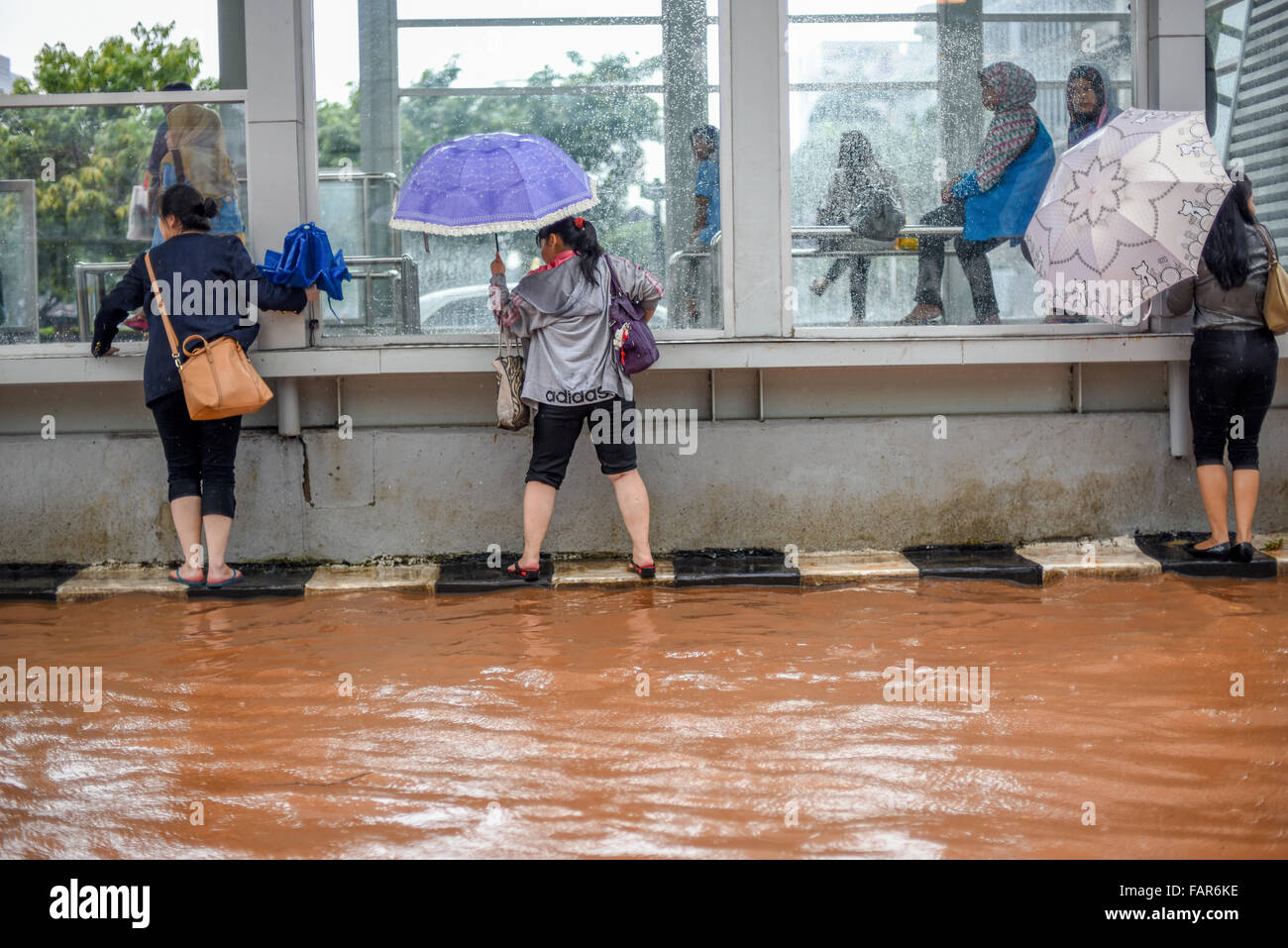 I pedoni cercano di evitare le acque alluvionali mentre camminano, appesi sul lato di una stazione degli autobus Trans Jakarta su Thamrin Street, Jakarta. Foto Stock