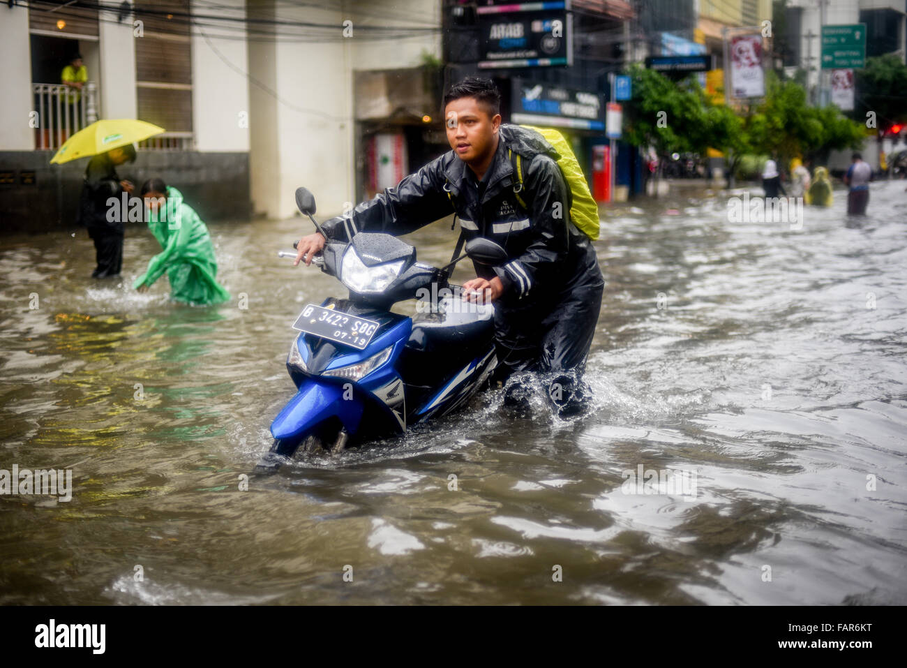 Un uomo che trasportava la sua moto attraverso l'acqua di Jakarta, dopo una pioggia continua ha lasciato la zona centrale della capitale indonesiana allagato. Foto Stock