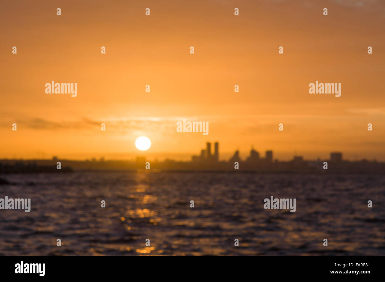 Immagine sfocata di silhouette della città prima del tramonto, onde in primo piano Foto Stock