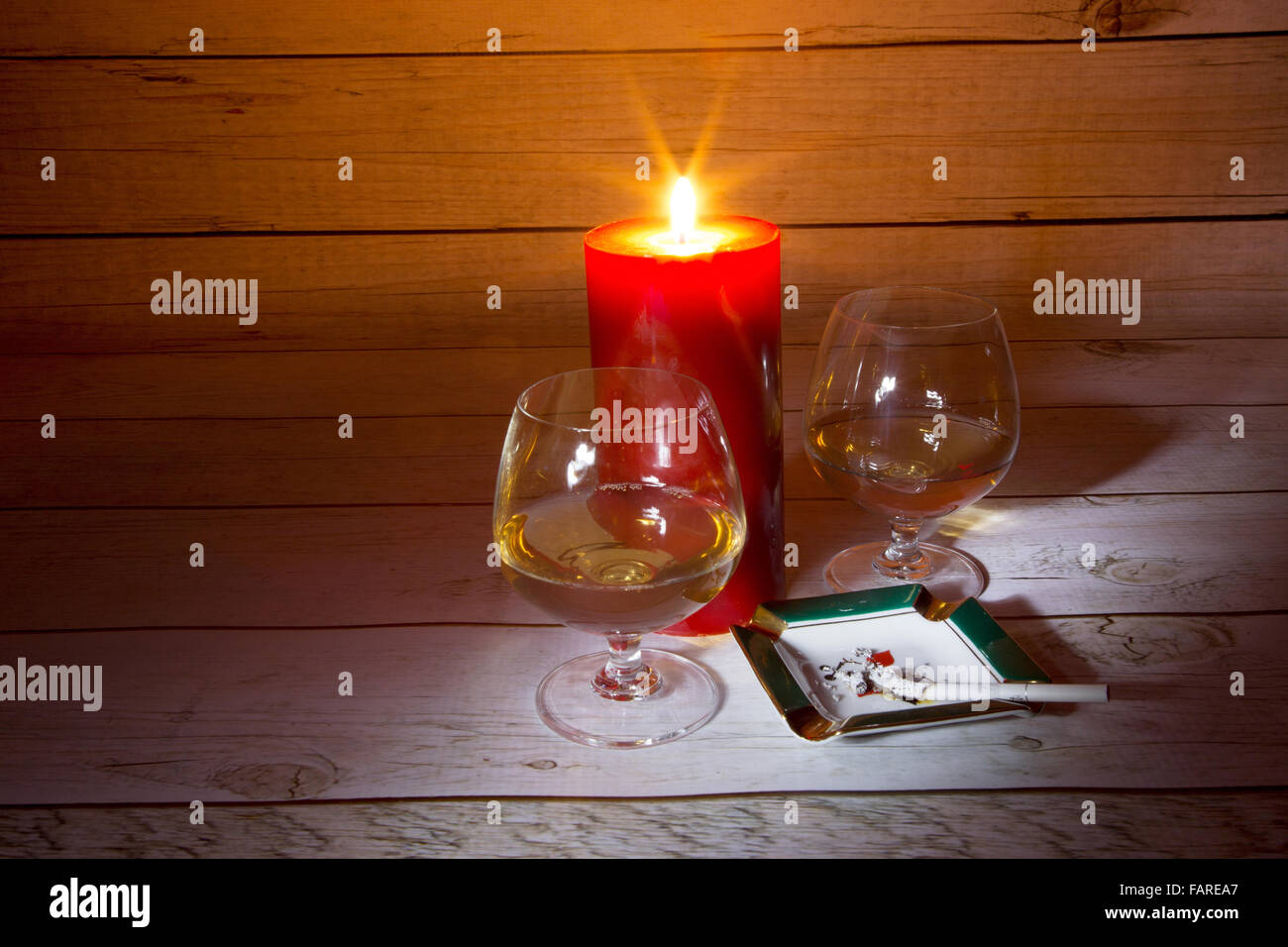 Due bicchieri di cognac, candele accese e la masterizzazione di sigaretta nel portacenere in una luce romantica sullo sfondo di un ta in legno Foto Stock