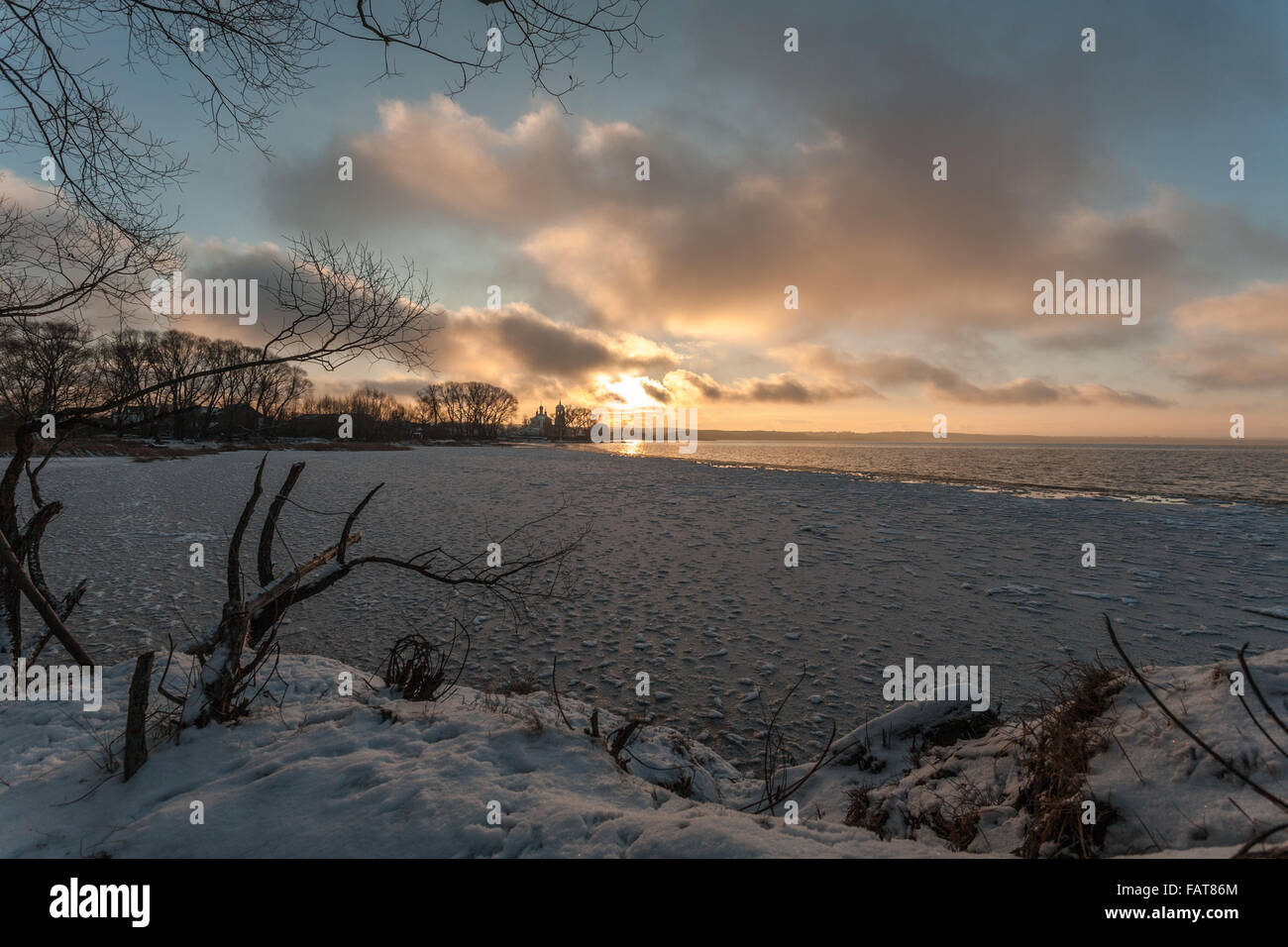 Il declino a freddo sulla banca del lago è in contrasto con i colori caldi del cielo e il sole Foto Stock