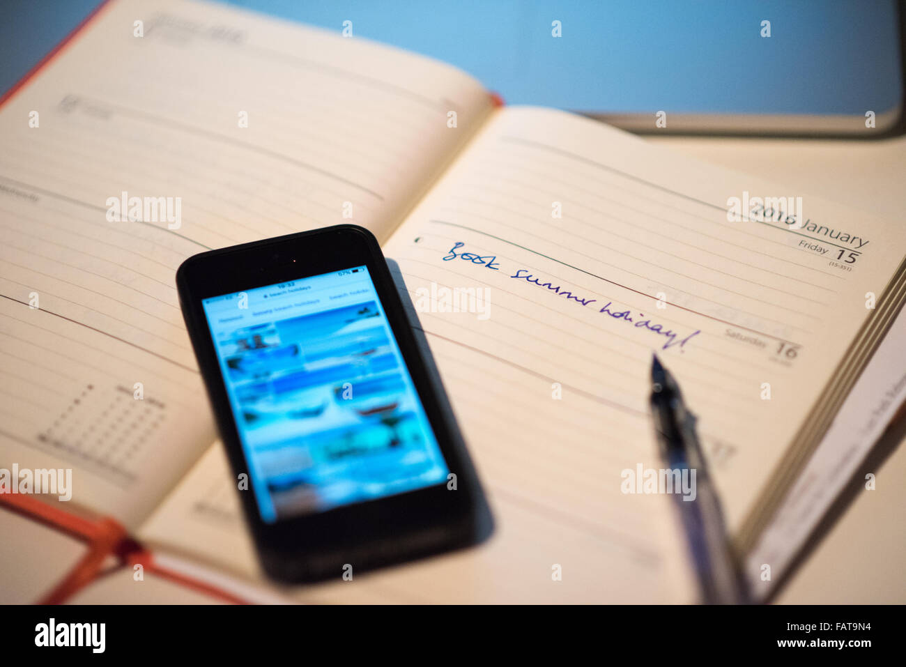 Un diario aperto con le parole del Libro vacanza estiva scarabocchiati su una pagina a fianco di uno smart phone con foto di pacchetti vacanze Foto Stock