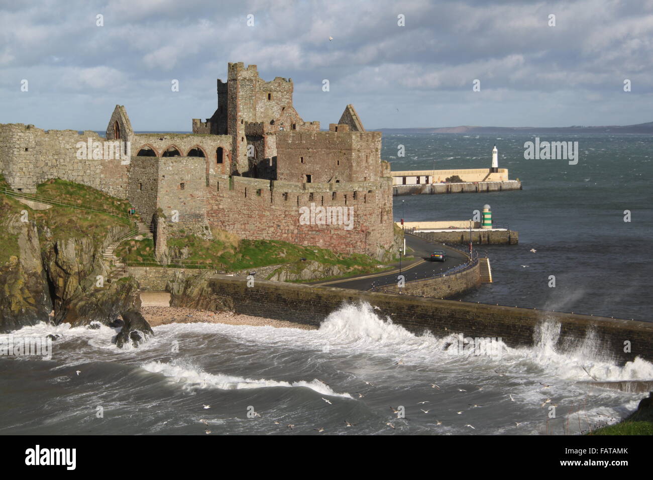 Il castello di pelare, sbucciare, Isola di Man con la baia e il molo in background. Onde infrangersi sulla spiaggia Fenella, parete protegge il porto. Foto Stock