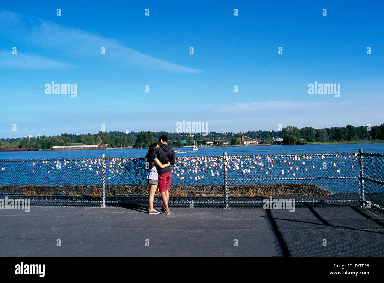 Coppia giovane in amore, amanti amore di fissaggio blocco / si blocca sulla staccionata lungo il fiume Fraser, New Westminster, British Columbia, Canada Foto Stock