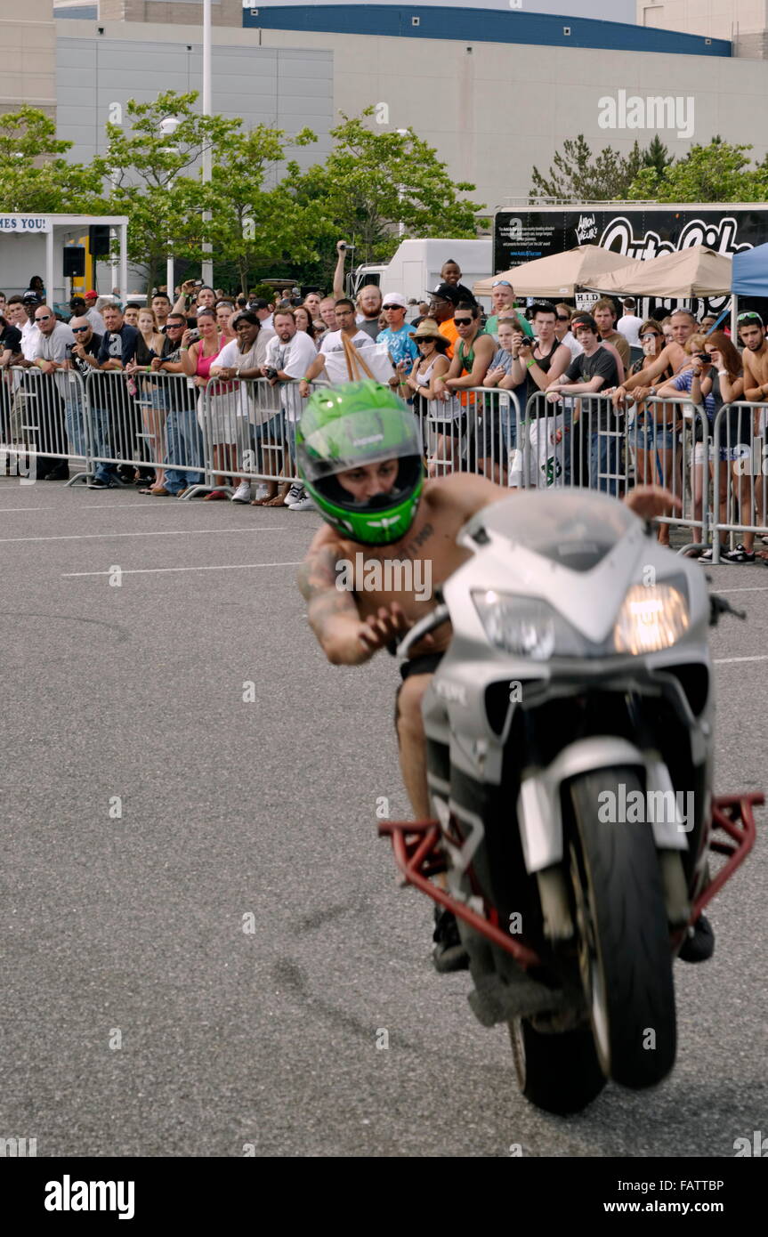 un motociclista che si esibiscono in un'acrobazie ti entusiasma una piccola folla con una ruota in uno spettacolo all'aperto. Foto Stock