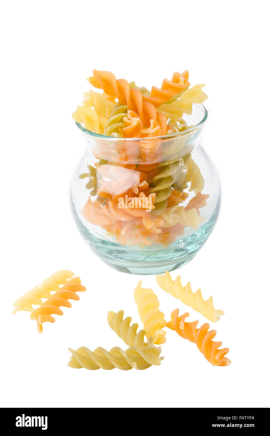 Non cotti pasta italiana - tre colori spirali in coppa di vetro su sfondo bianco. Foto Stock