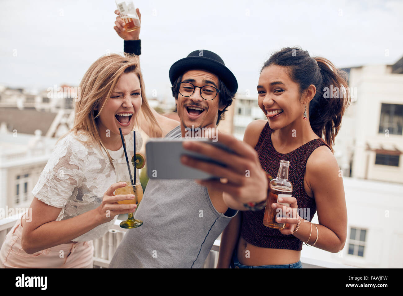 Piccolo gruppo di amici prendendo selfie su un telefono cellulare. Giovani uomini e donne con bevande rendendo divertente faccia tenendo un po di auto Foto Stock